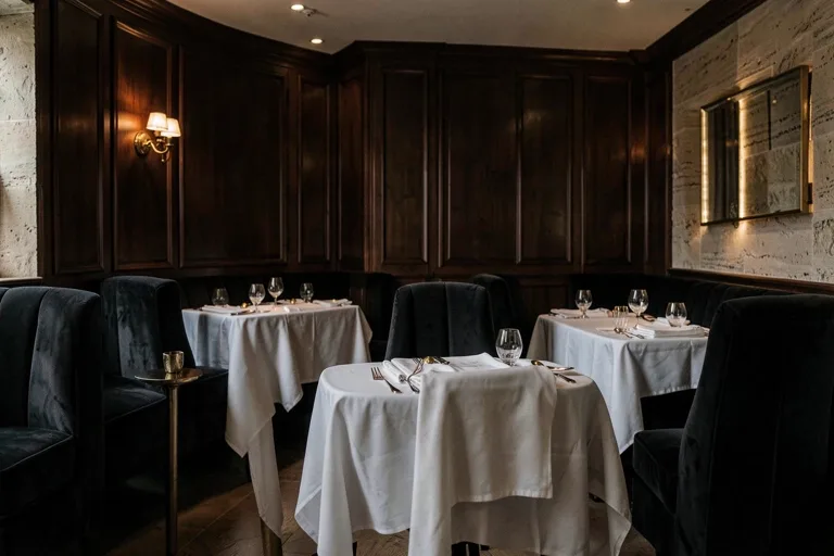 Restaurant gastronomique de luxe : boiseries en noyer, travertin, banquettes en velours et tables nappées de blanc en lumière chaude