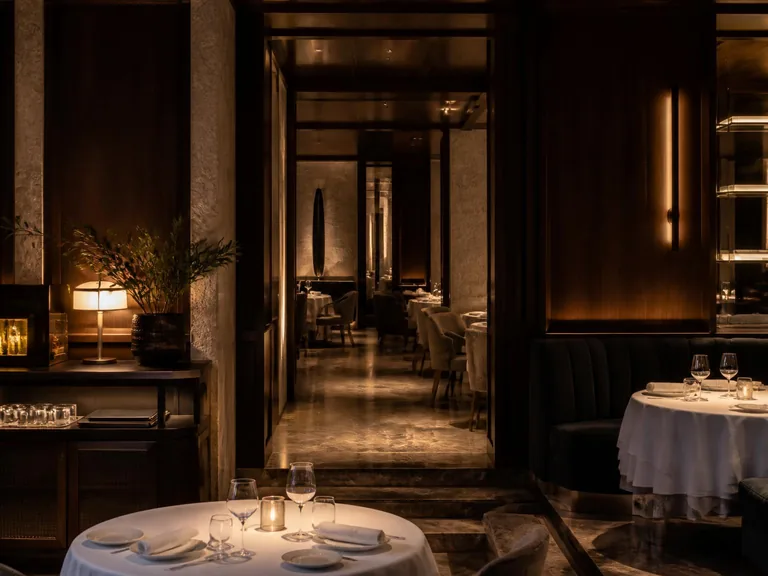 Restaurant gastronomique contemporain, noyer foncé, travertin, laiton brossé, banquettes en velours et tables nappées de blanc en lumière tamisée